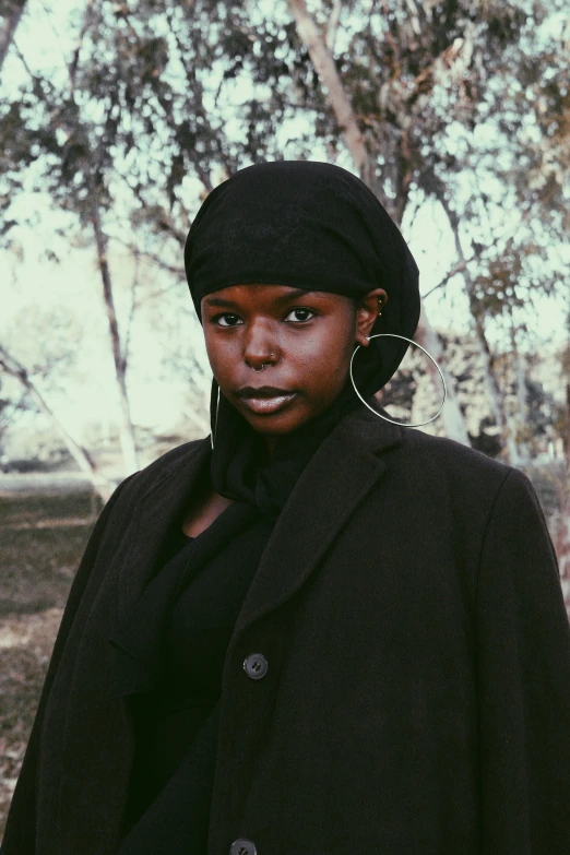 a woman standing in the middle of a forest, an album cover, by Nyuju Stumpy Brown, trending on unsplash, afrofuturism, face is wrapped in a black scarf, black stetson and coat, portrait androgynous girl, film still