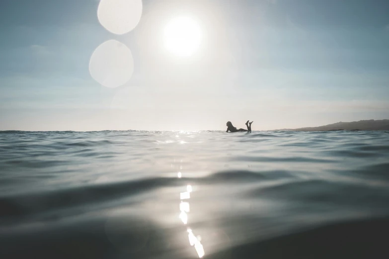 a person laying on a surfboard in the ocean, by Daniel Lieske, unsplash contest winner, sun flairs, subtle detailing, low quality photo, viewed from the ocean