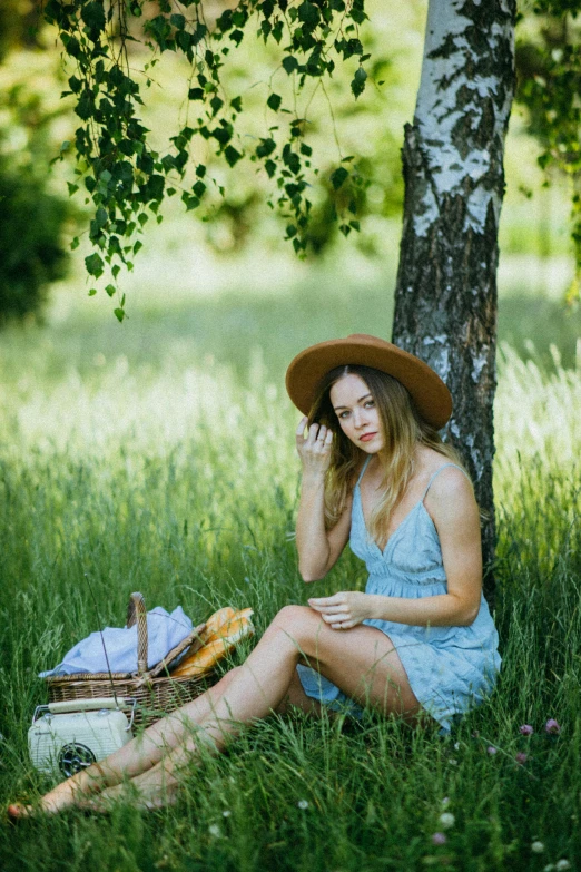 a woman sitting in the grass next to a tree, having a picnic, 5 0 0 px models, 2019 trending photo, with hat