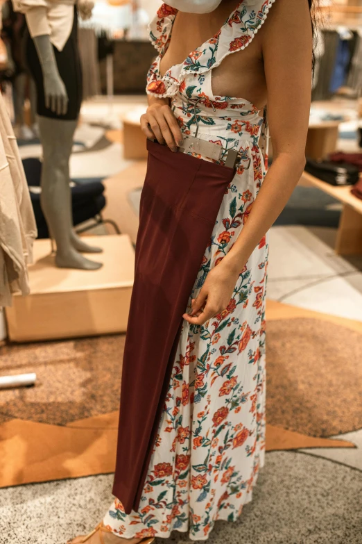 a woman standing next to a mannequin in a store, maroon accents, bottom body close up, floral, exposed waist