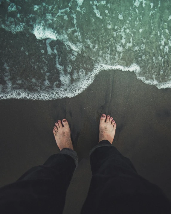 a person standing on a beach next to the ocean, wet feet in water, lgbtq, from above, instagram photo