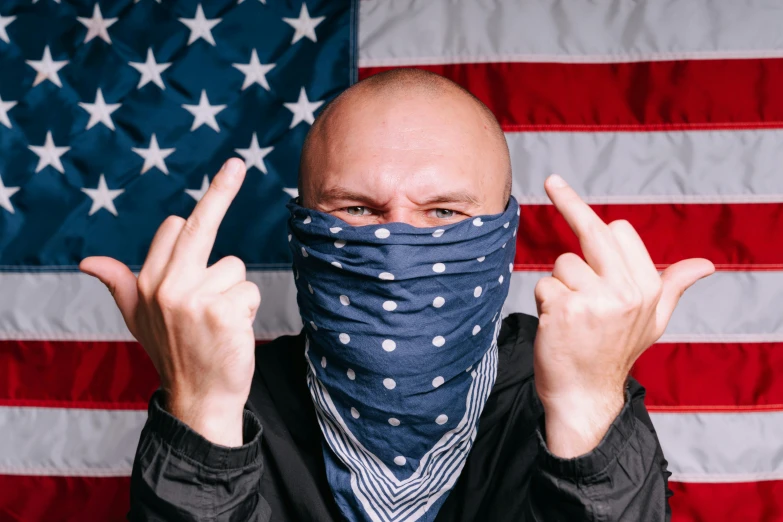 a bald man wearing a bandana in front of an american flag, inspired by Brian 'Chippy' Dugan, unsplash, stuckism, threatening pose, cloak covering face, surgical mask covering mouth, with pointing finger