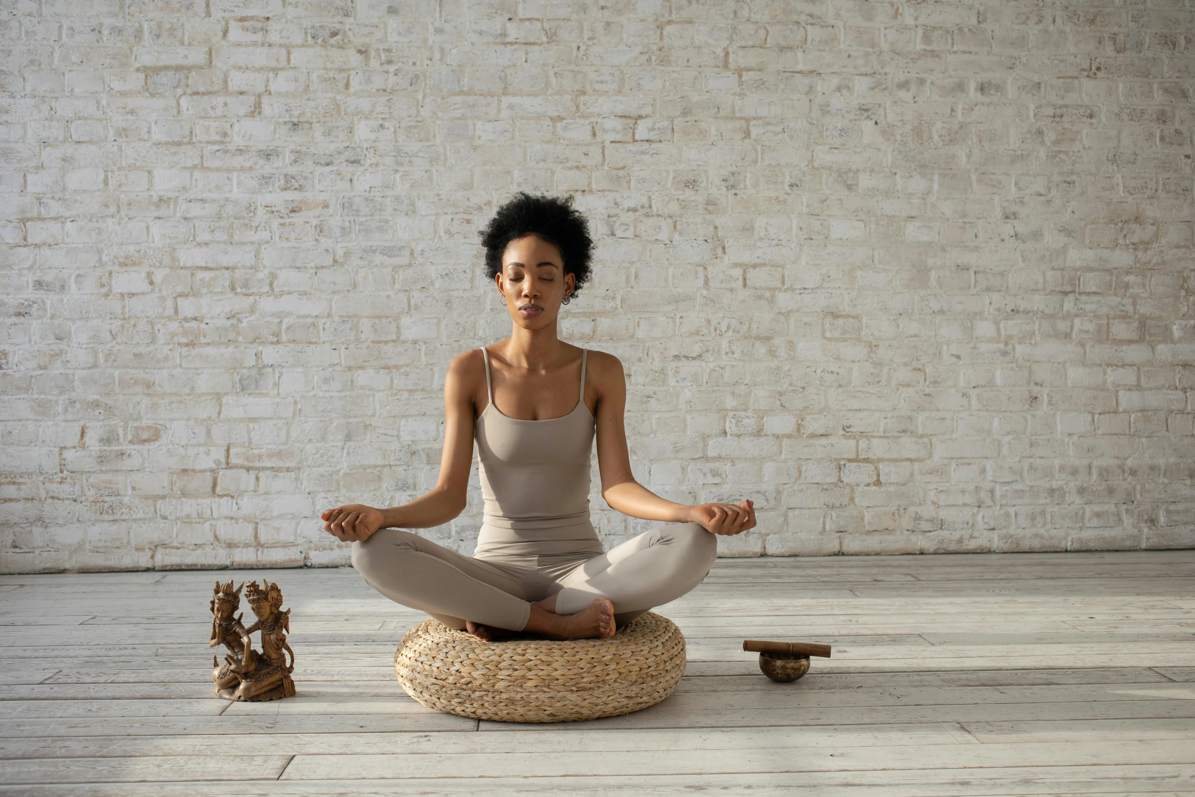 a woman sitting in a meditation position in front of a brick wall, trending on pexels, figuration libre, sitting on a mocha-colored table, uk, on a wooden plate, “ full body