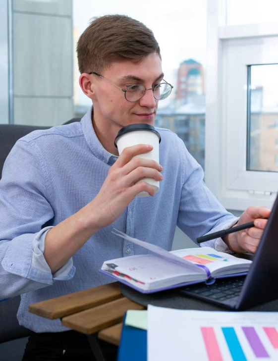 a man sitting at a desk with a laptop and a cup of coffee, a screenshot, trending on pexels, lgbt, very nerdy, russian academic, non binary model
