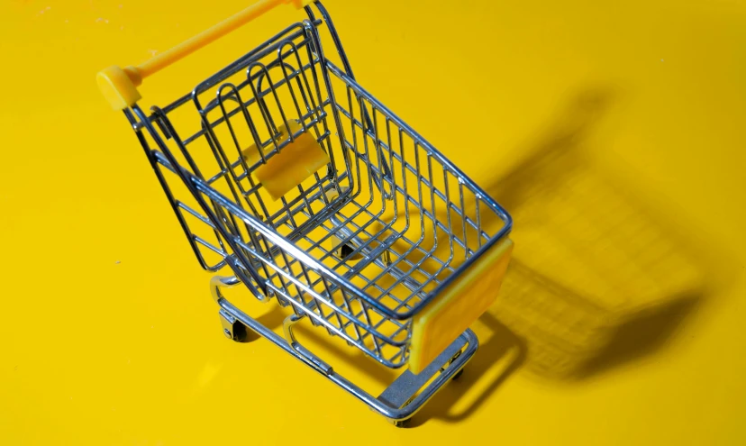 a miniature shopping cart on a yellow surface, by Adam Marczyński, pexels, hyperrealism, silver, square, glossy yellow,