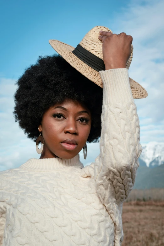 a woman standing in a field with a hat on her head, trending on pexels, afrofuturism, white sweater, portrait”, promotional image, big hair