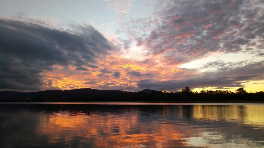 a large body of water under a cloudy sky, orange and red sky, lachlan bailey, view from the lake, orange and blue sky