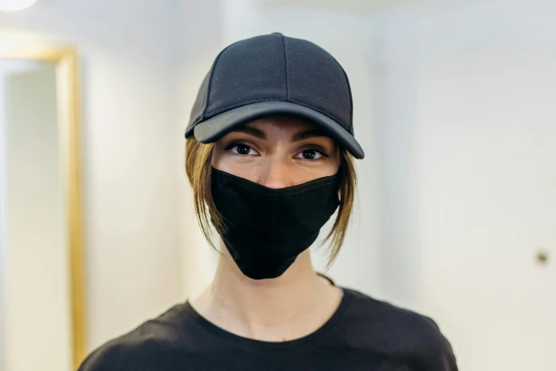 a woman wearing a black face mask and a baseball cap, slight stubble, avant designer uniform, thumbnail, commercially ready