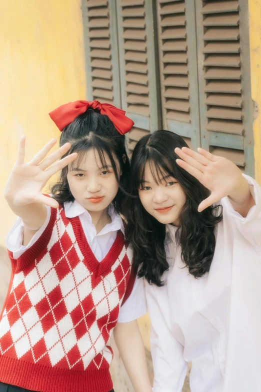 a couple of women standing next to each other, an album cover, by Tan Ting-pho, unsplash, wearing a school uniform, red contact lenses, wave a hand at the camera, bowknot