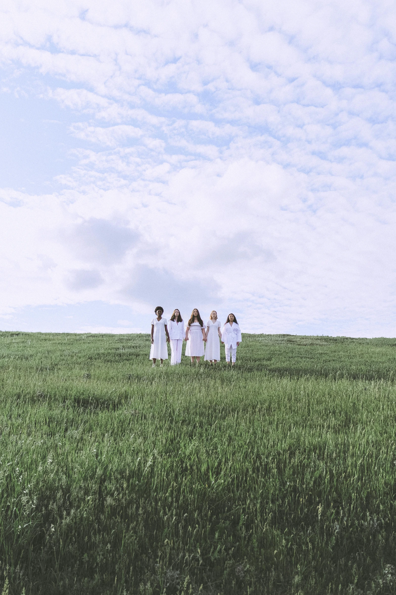 a group of people standing on top of a lush green field, an album cover, inspired by Pierre Puvis de Chavannes, unsplash, land art, white clothing, young women, white sky, round-cropped