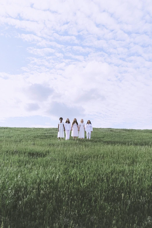 a group of people standing on top of a lush green field, an album cover, inspired by Pierre Puvis de Chavannes, unsplash, land art, white clothing, young women, white sky, round-cropped