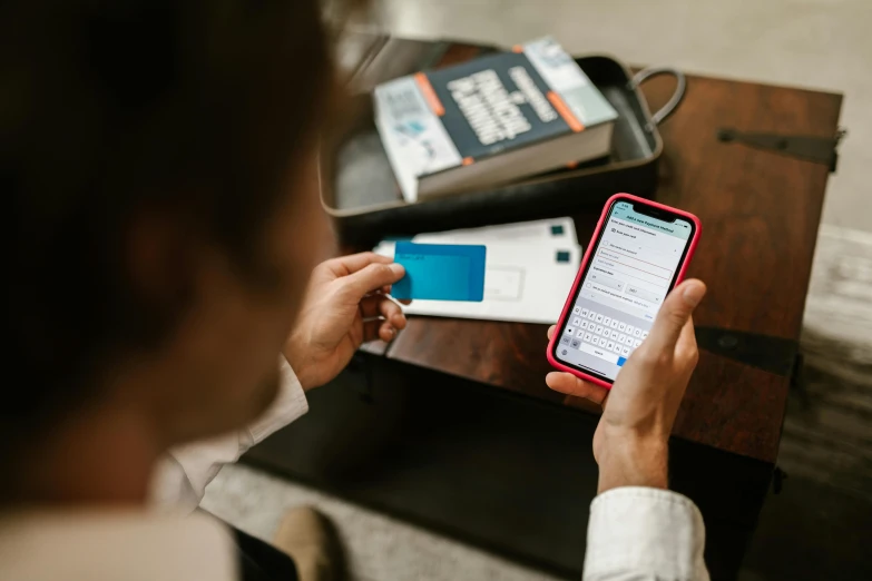 a person sitting at a table with a cell phone, holding a book, pair of keycards on table, taken on iphone 14 pro, high res photo