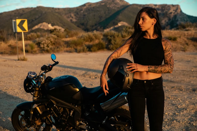 a woman standing next to a motorcycle in the desert, by Lee Loughridge, pexels contest winner, symbolism, wearing a black cropped tank top, with tattoos, ayne haag, charli bowater and artgeem