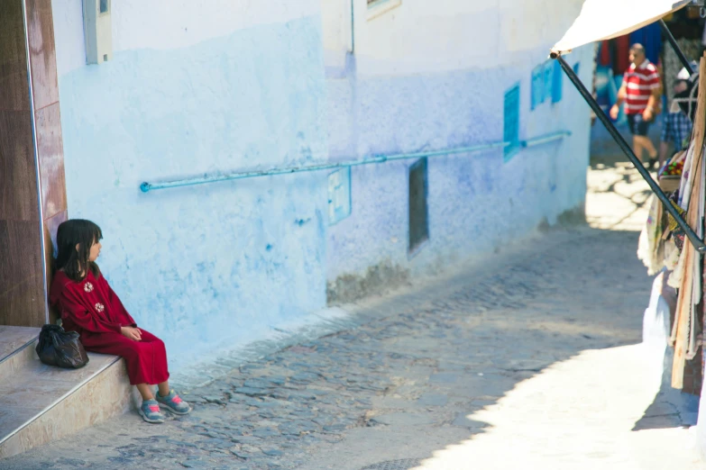 a little girl sitting on the steps of a building, inspired by Steve McCurry, pexels contest winner, tuareg, blue and red, in a village street, avatar image