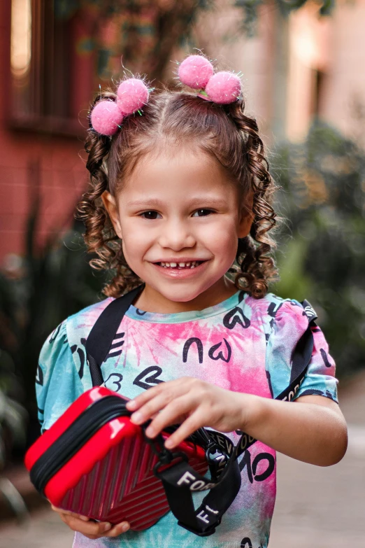 a little girl in a tie dye shirt holding a red suitcase, by Lucia Peka, happening, curly bangs and ponytail, alanis guillen, medium close up portrait, serving happy meals