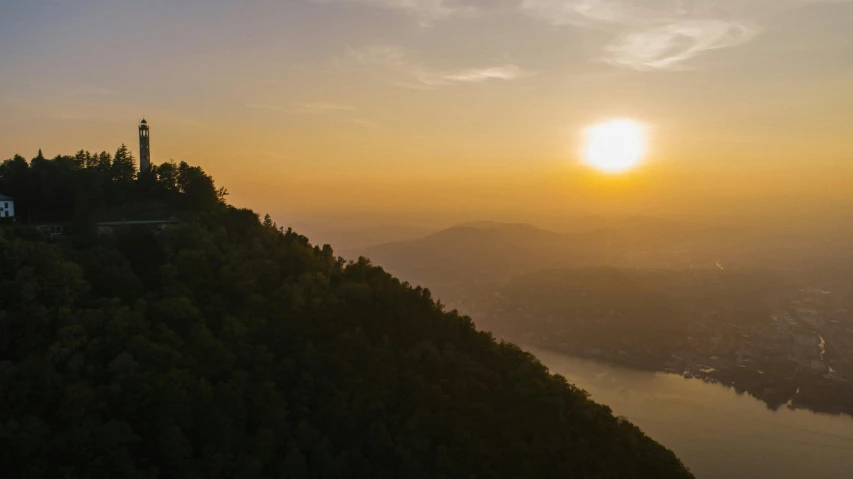 a lighthouse sitting on top of a hill next to a body of water, pexels contest winner, sumatraism, sun rises between two mountains, guwahati, 4 k cinematic panoramic view, overlooking a valley with trees