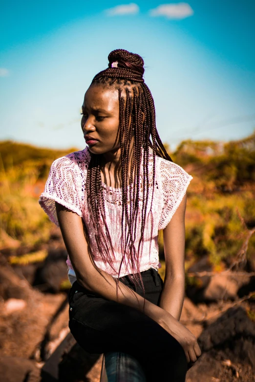 a woman sitting on top of a pile of rocks, inspired by Ras Akyem, trending on pexels, afrofuturism, long braided hair pulled back, dslr 5 0 mm portrait photo, standing in the savannah, bright vivid colours