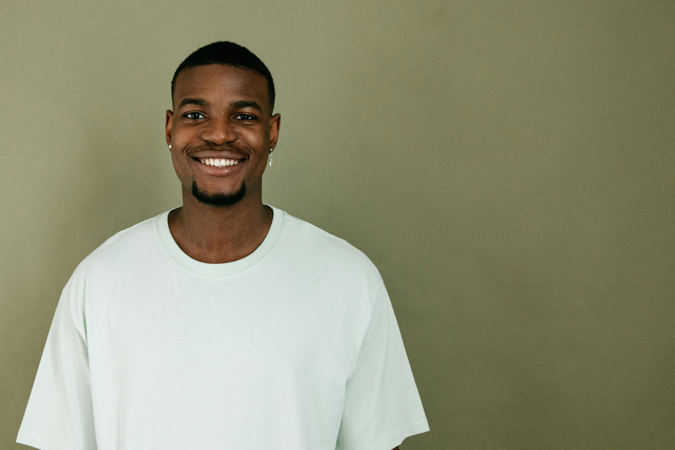 a man in a white shirt smiles at the camera, inspired by Paul Georges, pexels contest winner, hurufiyya, jaylen brown, plain background, greenish skin, full view blank background