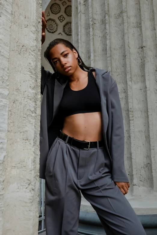 a woman leaning against a wall in front of a building, trending on pexels, renaissance, wearing black grey suit, wearing a crop top, bra and shorts streetwear, african american young woman