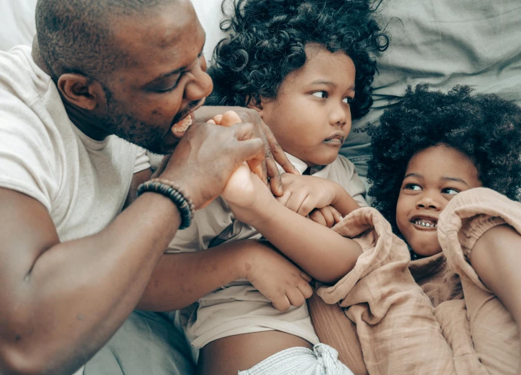 a man and two children laying on a bed, pexels contest winner, black man with afro hair, holding each other hands, profile image, thumbnail