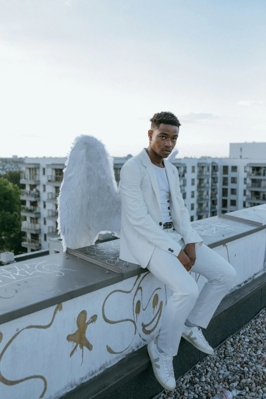 a man in a white suit sitting on a ledge, an album cover, by Cosmo Alexander, pexels contest winner, angelic wings, berlin fashion, black teenage boy, promotional image