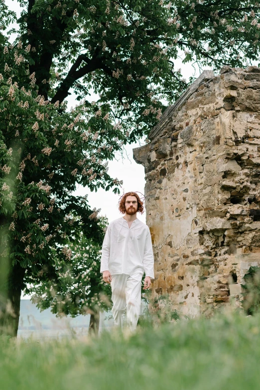 a man that is standing in the grass, an album cover, inspired by Apollinary Vasnetsov, unsplash, renaissance, wearing white pajamas, walking in a castle, press shot, performance