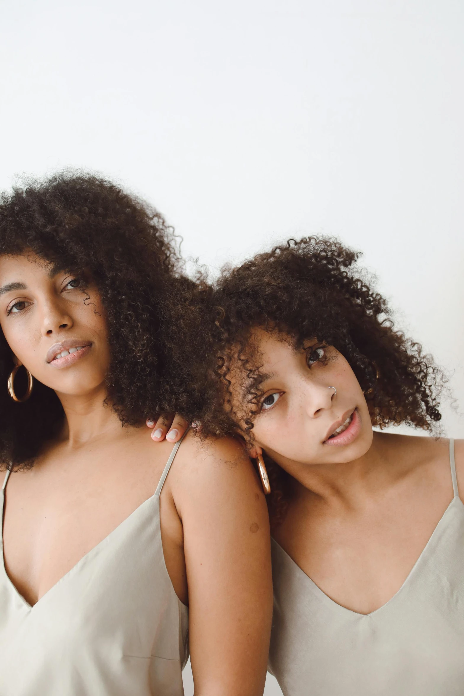 a couple of women standing next to each other, by Lily Delissa Joseph, trending on pexels, renaissance, curls on top, muted brown, product introduction photo, gray skin