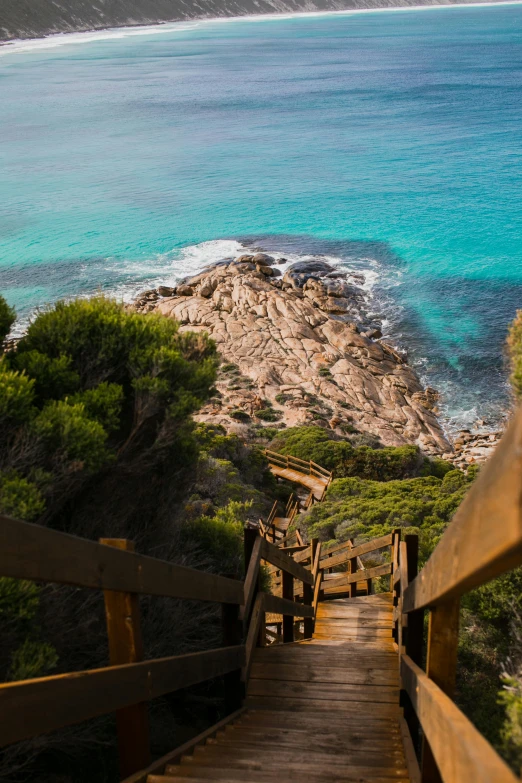 a wooden staircase going down to the beach, by Peter Churcher, trending on pexels, rocky terrain, turquoise water, view from high, ben nicholas