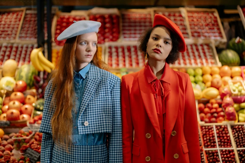 two women standing next to each other in front of a fruit stand, by Anita Malfatti, trending on pexels, renaissance, brutalist fashion show, red and blue garments, berets, sadie sink