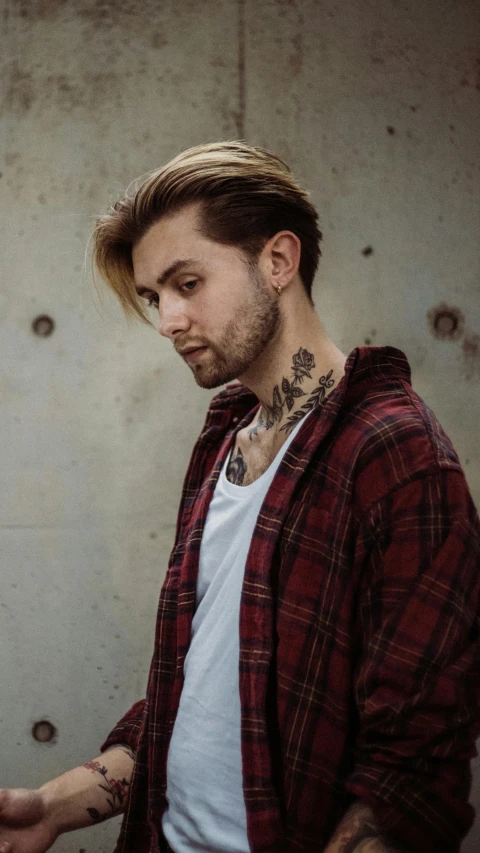 a man standing in front of a concrete wall, a tattoo, trending on pexels, wearing a flannel shirt, long swept back blond hair, andrzej marszalek, ash thorp