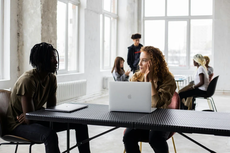 a group of people sitting around a table with laptops, by Carey Morris, trending on pexels, female looking, medium shot of two characters, student, looking off to the side