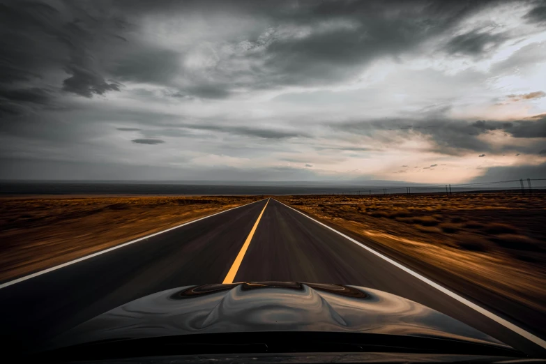 a car driving down a road under a cloudy sky, by Daniel Seghers, unsplash, visual art, looking onto the horizon, transparent black windshield, new mexico, high forehead