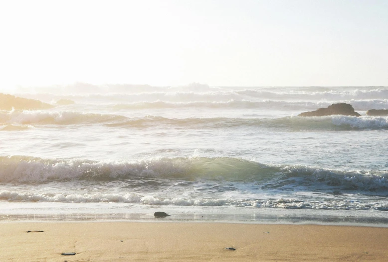 a man riding a surfboard on top of a sandy beach, a picture, inspired by William Trost Richards, unsplash, hazy water, glistening seafoam, morning sunlight, hollister ranch