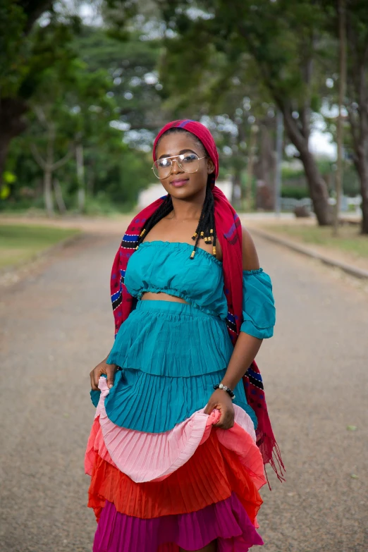 a woman standing in the middle of a road, an album cover, inspired by Ras Akyem, teal and pink, wearing an african dress, post graduate, red and blue garments