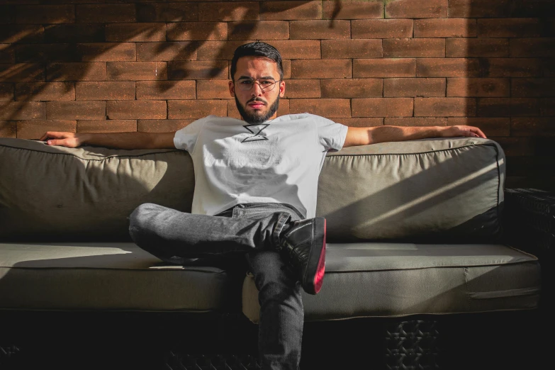 a man sitting on a couch in front of a brick wall, inspired by Nathan Oliveira, pexels contest winner, les nabis, wearing pants and a t-shirt, avatar image, mohamed chahin style, profile pic