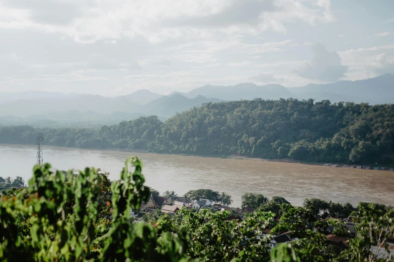 a view of a river with mountains in the background, by Daniel Lieske, unsplash contest winner, sumatraism, imperial city in the distance, overlooking a valley with trees, slight haze, jen atkin