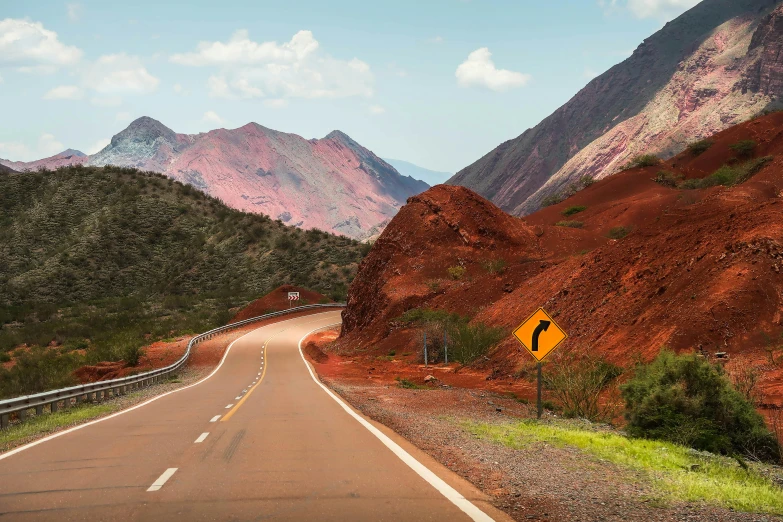 a yellow sign sitting on the side of a road, inspired by Steve McCurry, pexels contest winner, magic realism, landscape with red mountains, copper veins, andes, curvacious