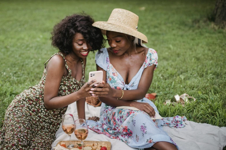 two women sitting on a blanket looking at a cell phone, a photo, trending on pexels, figuration libre, brown skin like soil, wearing a sundress, wine, gardening