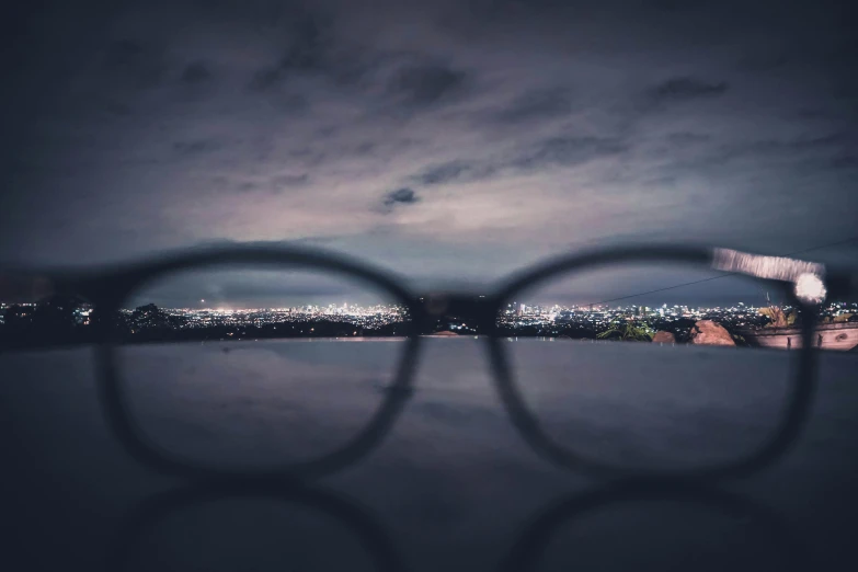 a pair of glasses sitting on top of a table, a picture, by Adam Marczyński, trending on pexels, gloomy lights in the sky, view from eyes, peering over from his heavy, spectacled