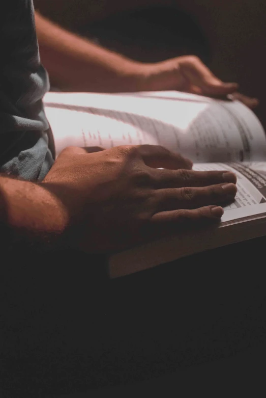 a person sitting on a couch reading a book, by Scott Gustafson, pexels, happening, prayer hands, low key light, he is holding a large book, scientific study