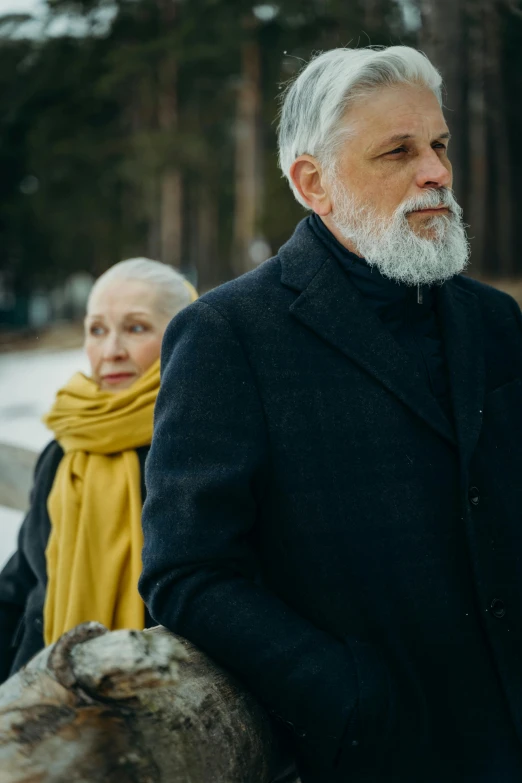 a man in a black coat standing next to a woman in a yellow scarf, a portrait, by Grytė Pintukaitė, pexels contest winner, silver hair and beard, from the tusk movie, wandering, promotional image