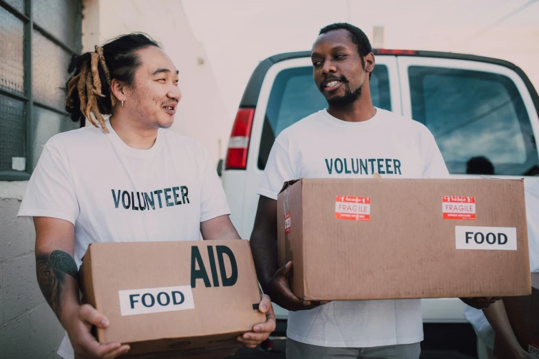 two people holding boxes in front of a van, by Francis Helps, food, background image, diverse, a friend in need