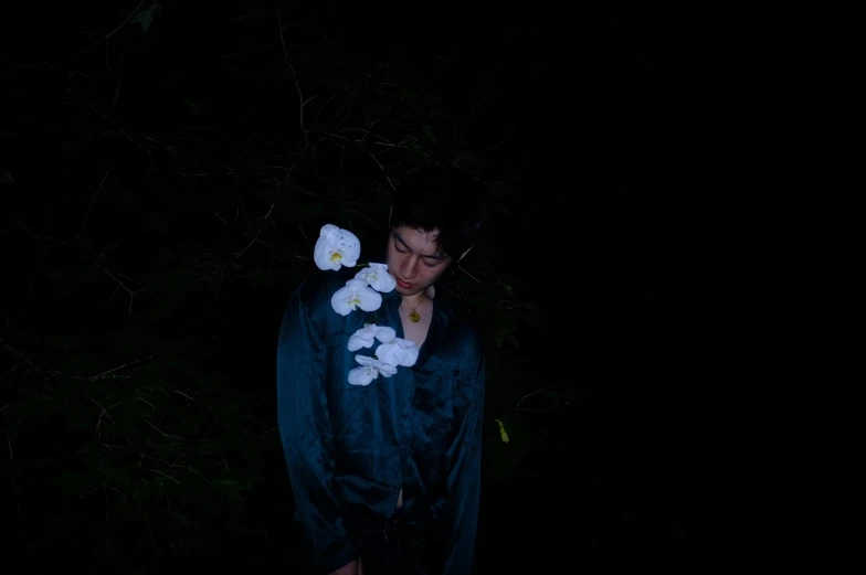 a man standing in the dark with flowers in his hair, an album cover, unsplash, aoi ogata, bella poarch, ignant, high quality photo