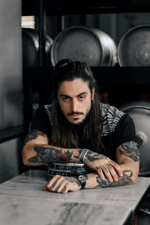 a man with long hair sitting at a table, a tattoo, by Adam Dario Keel, bartending, 1 / 2 headshot, promo image, gif