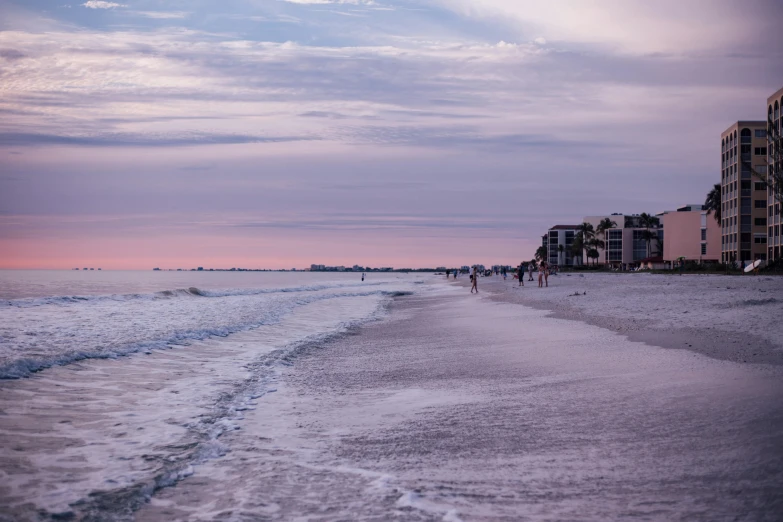 a group of people walking along a beach next to the ocean, by Carey Morris, pexels contest winner, renaissance, soft lilac skies, neighborhood, the emerald coast, twilight ; wide shot