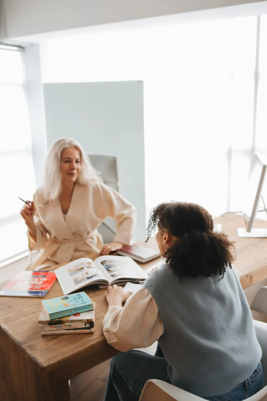 two women sitting at a table in front of a window, pexels contest winner, art & language, textbooks and books, blonde, talking, professional modeling