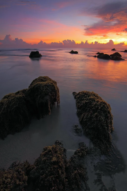 a couple of rocks sitting on top of a sandy beach, during a sunset, indonesia national geographic, reefs