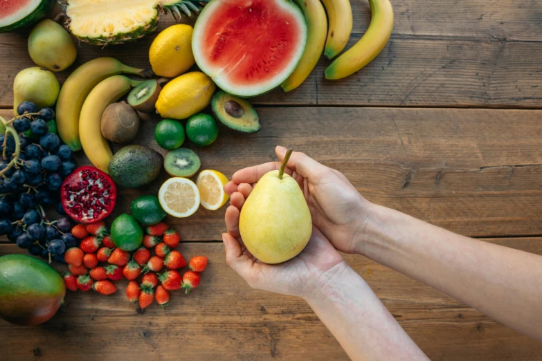 a person holding a piece of fruit on top of a wooden table, background image, multicoloured, different sizes, thumbnail