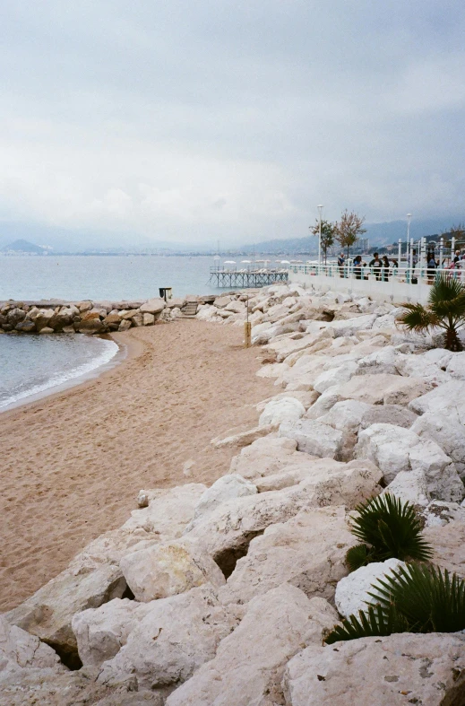 a sandy beach next to a body of water, inspired by Jean-Yves Couliou, romanticism, cannes, limestone, port, overcast