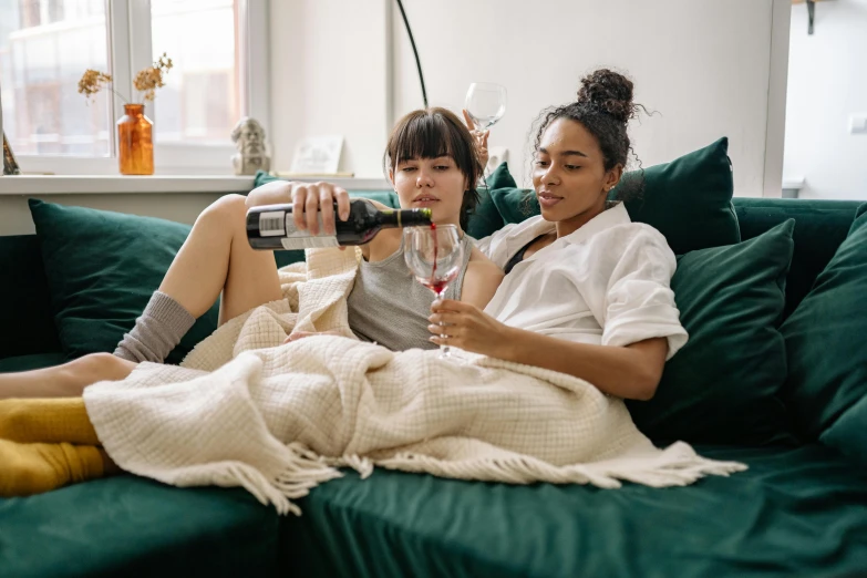 a couple of women sitting on top of a green couch, pexels contest winner, happening, with a bottle of wine, sitting on a bed, holding a drink, profile image